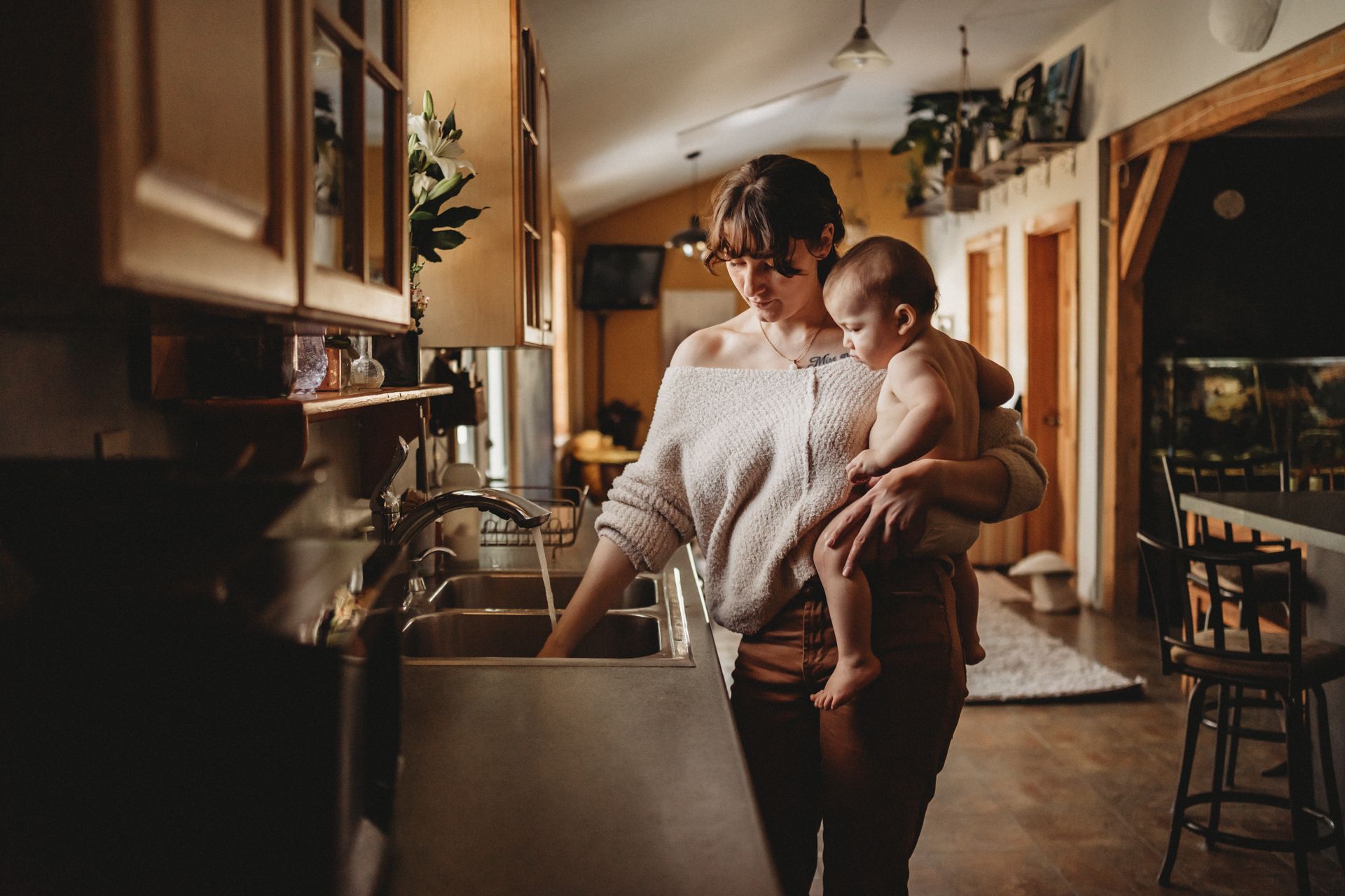 A cozy kitchen scene showing someone holding a child while working at the counter.