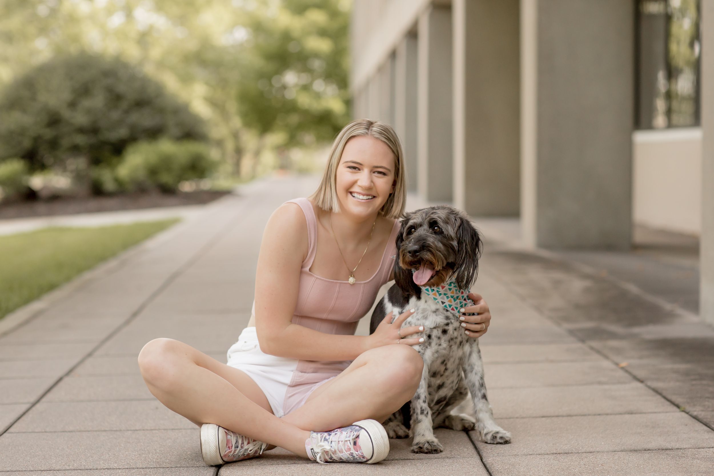 Happy young blonde woman sitting outdoors with spotted dog on sunny day.