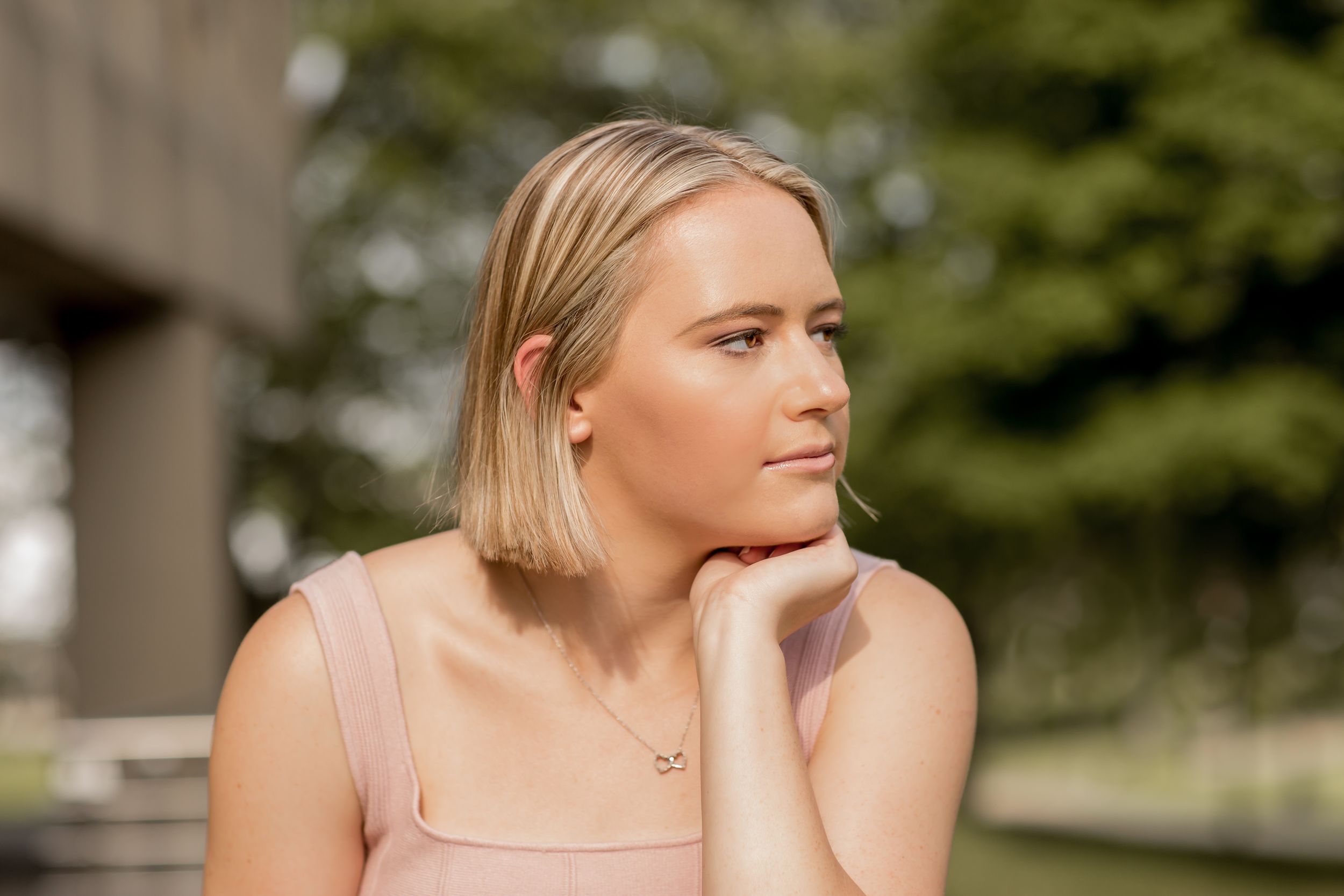 Young blonde woman with bob haircut resting chin on hand in outdoor portrait.