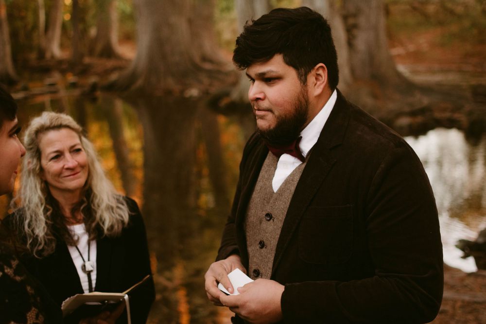 Wedding ceremony in autumn forest with officiant and groom during emotional moment.