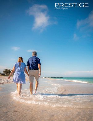 Couple walking hand in hand on beach at sunset wearing blue and beige casual attire.