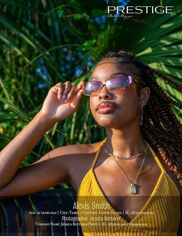 Stylish sunglasses and jewelry complement yellow top against tropical foliage background.