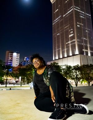 A nighttime portrait of someone in sequins posing against illuminated city buildings.