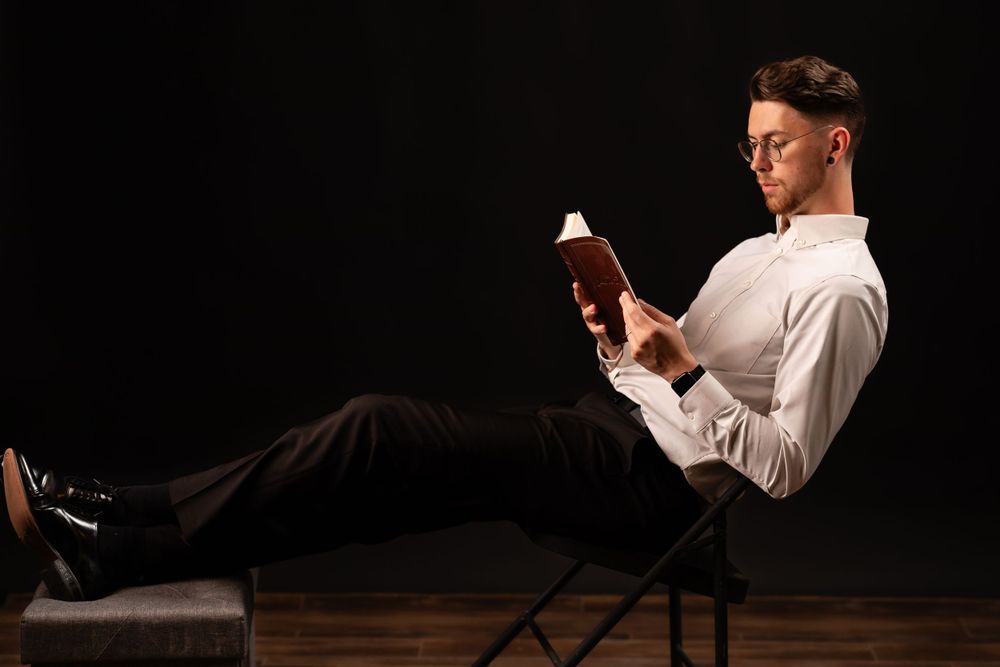 Person reading book while relaxing in chair against dark background.