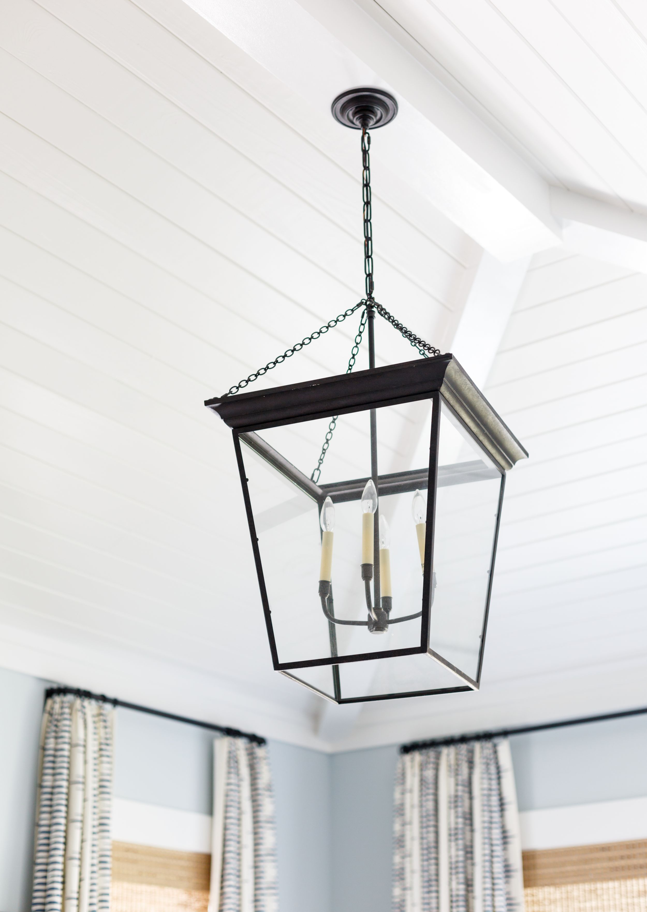 Visual comfort iron pendant hanging from tongue and groove ceiling.