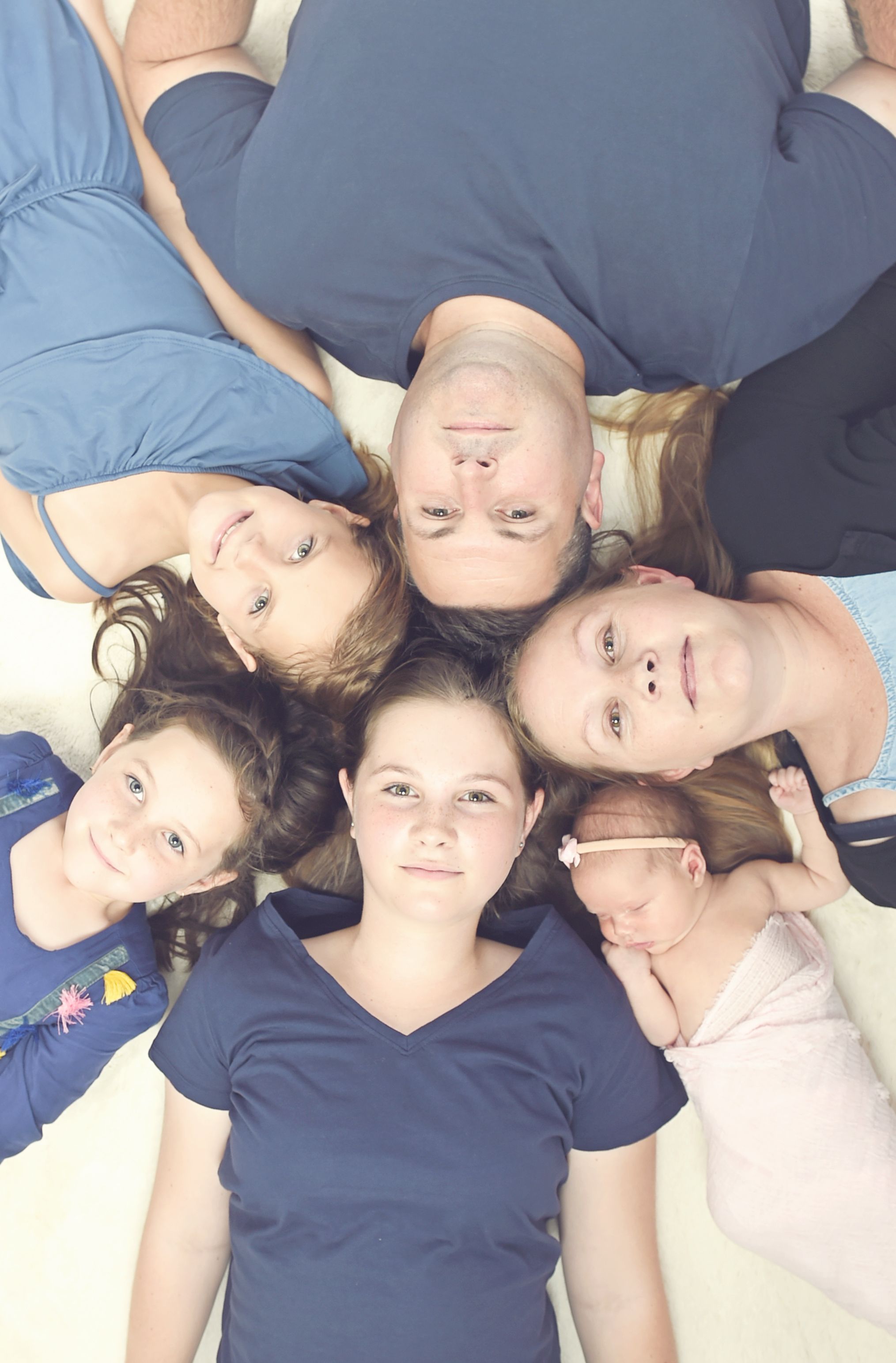 Family laying on floor looking up at camera with heads together