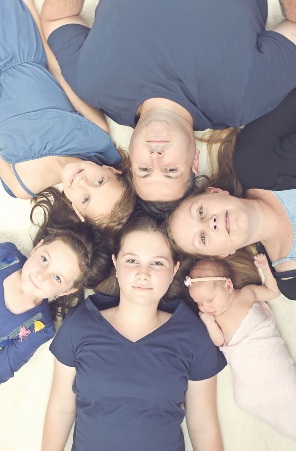 Family laying on floor looking up at camera with heads together