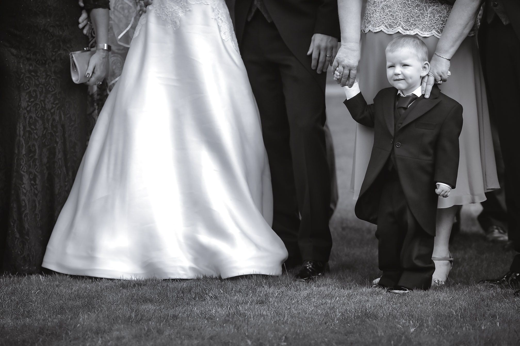 A small child in formal attire stands by a flowing white wedding dress in black and white photography.