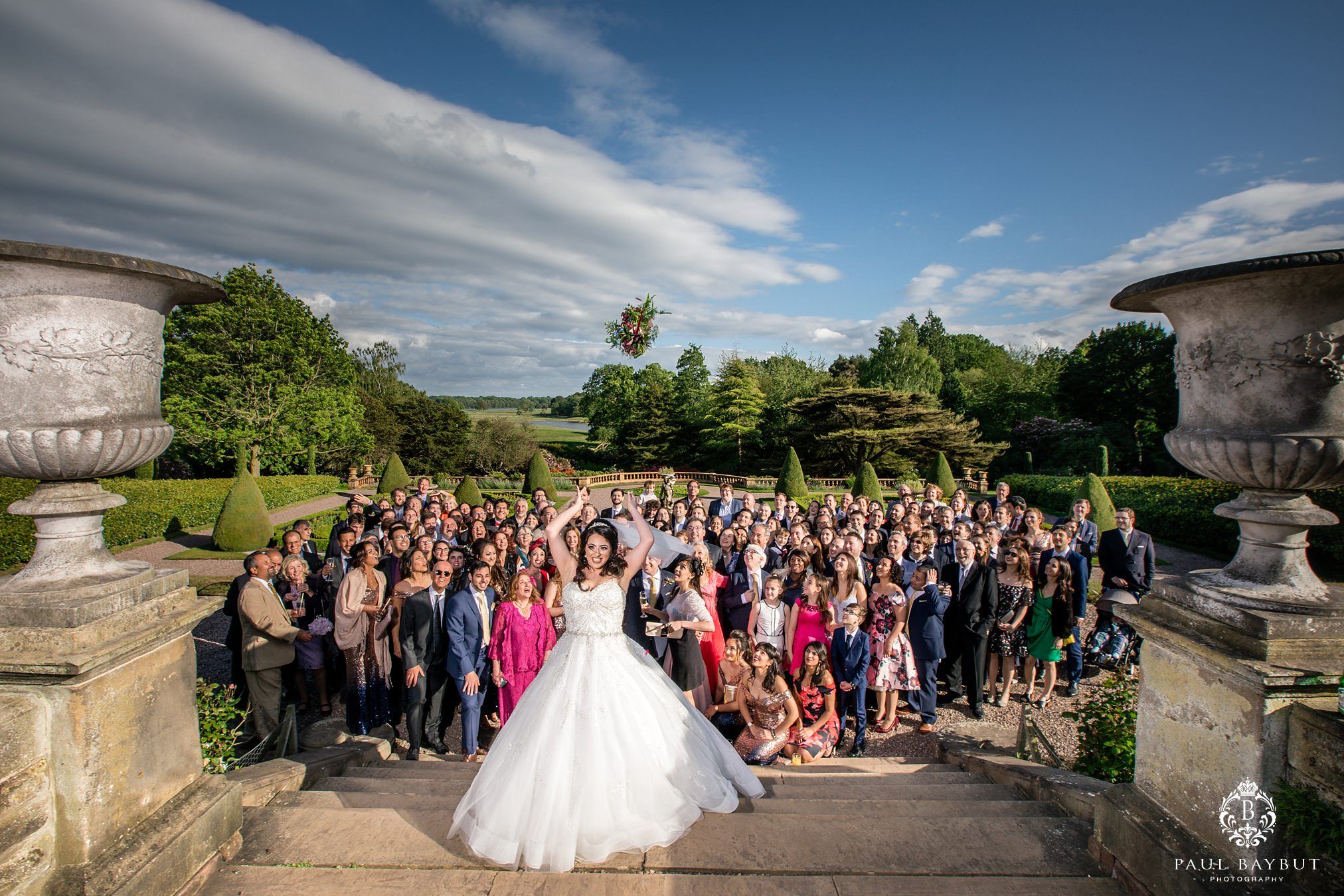 Aerial view of large wedding gathering on stone terrace with dramatic cloudscape.