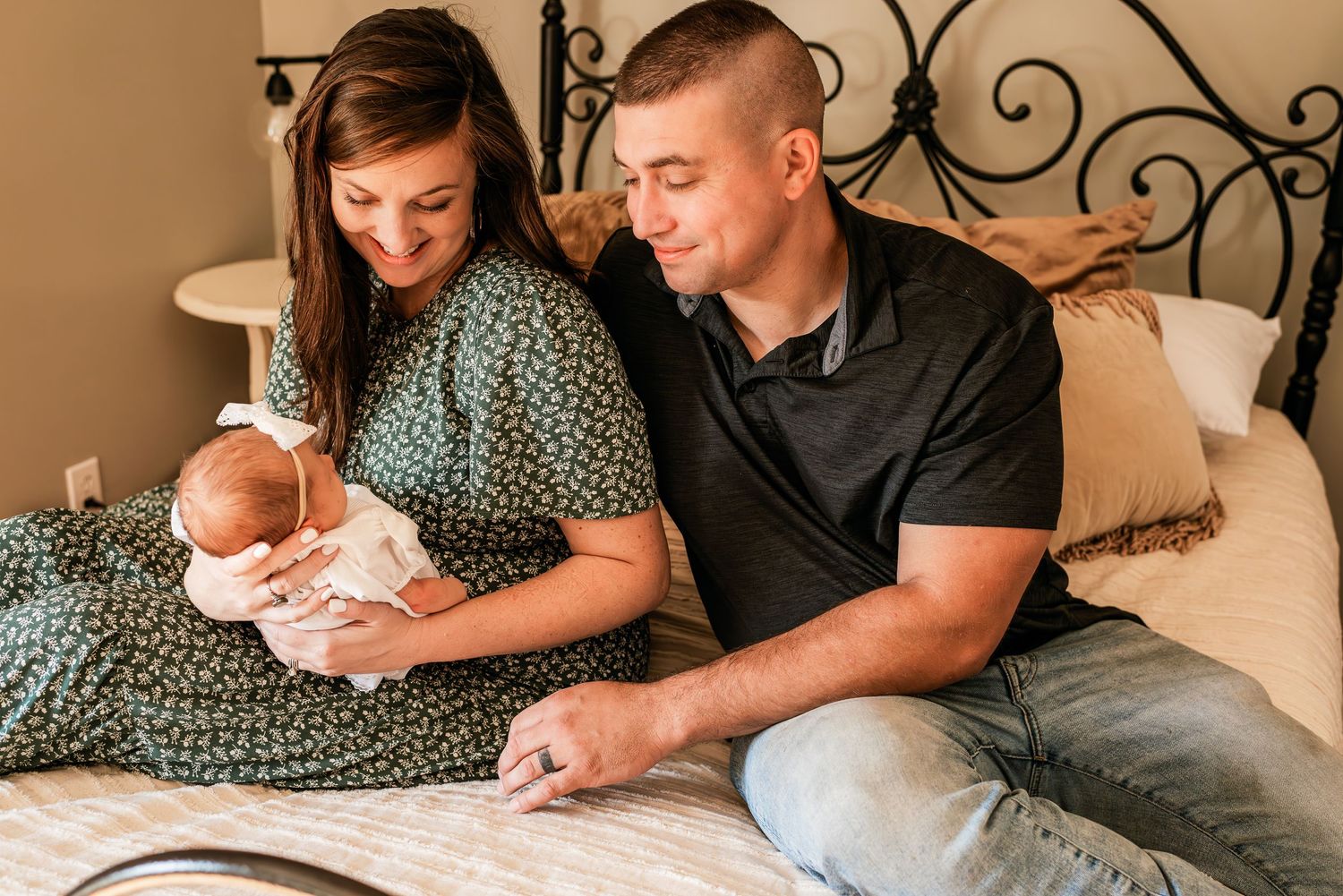 A tender moment as parents bond with their newborn baby while sitting together on a bed with decorative headboard.