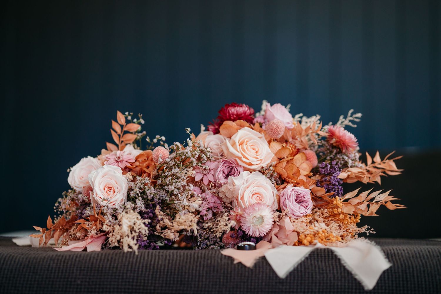 Decorative floral arrangement with pink roses and autumn-colored foliage against dark background.