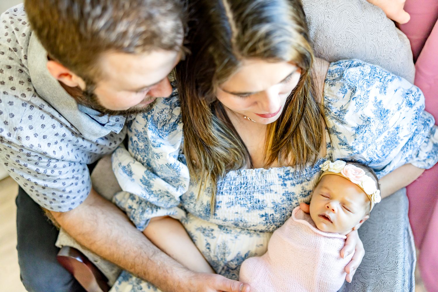 Mom snuggles baby girl in chair while dad hugs her during newborn photos in Colorado Springs.