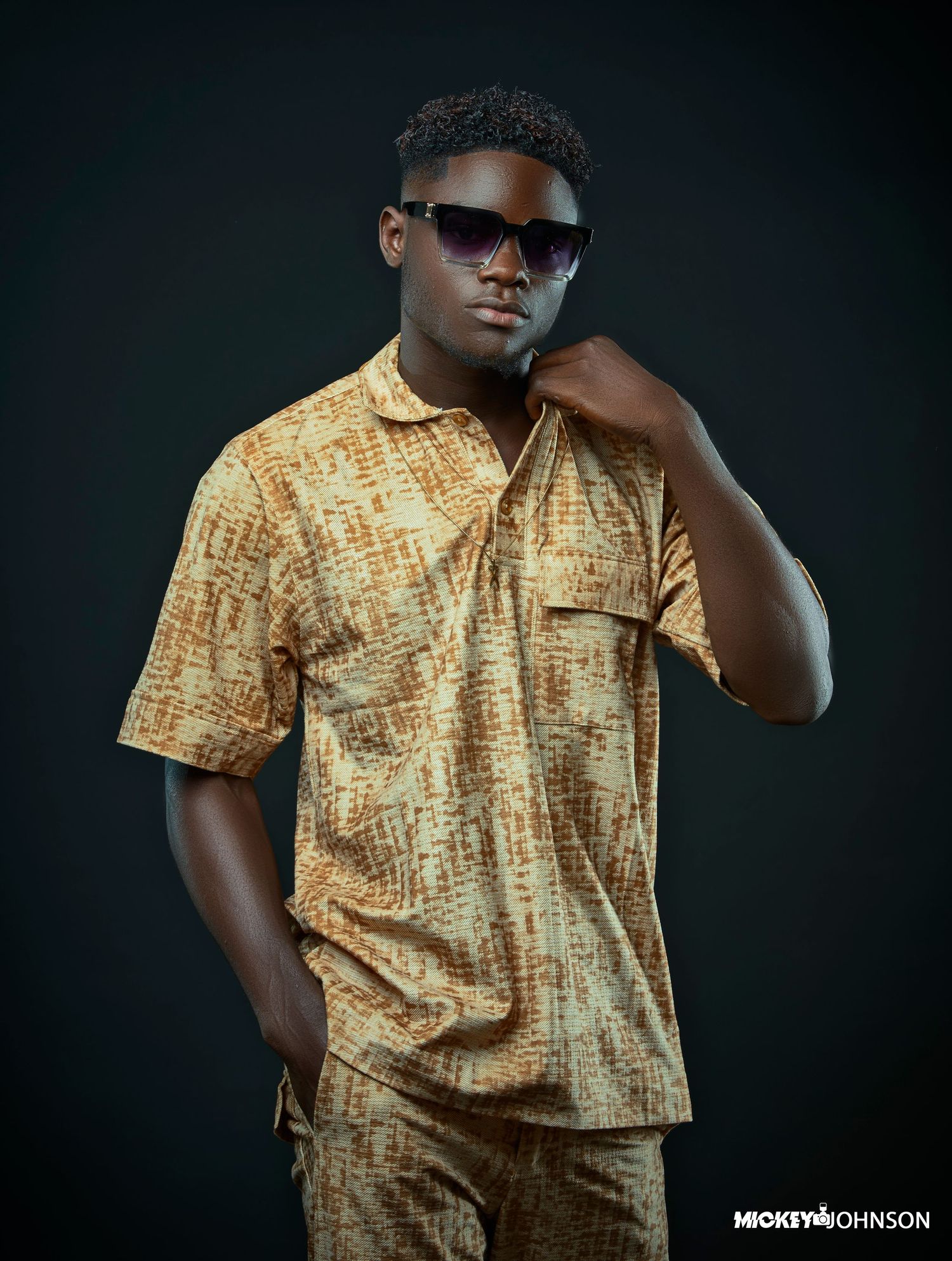 Studio portrait featuring yellow patterned shirt against dark background.