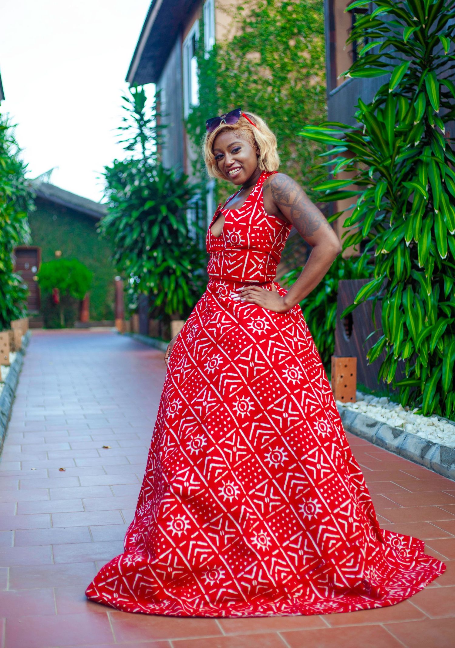 Red geometric patterned ballgown photographed in outdoor garden setting with stone pathway.