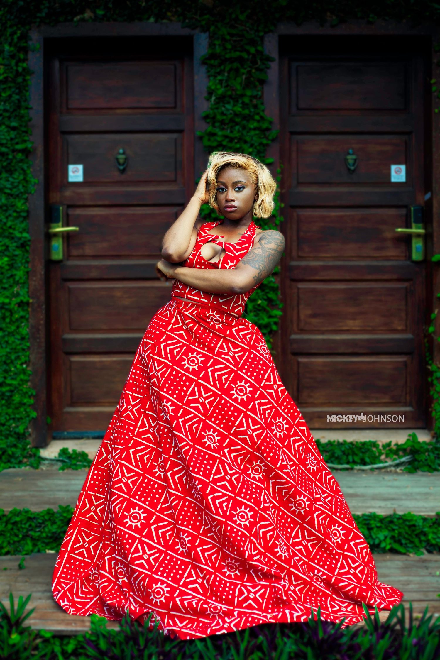 Fashion model poses in vibrant red and white geometric print maxi dress against wooden door backdrop.