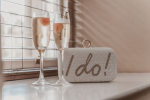 Two champagne glasses next to a white beaded clutch purse with 'I do' text.