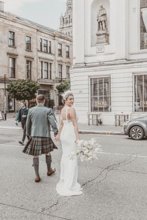 Wedding scene on a city street with traditional Scottish kilt and elegant white dress.