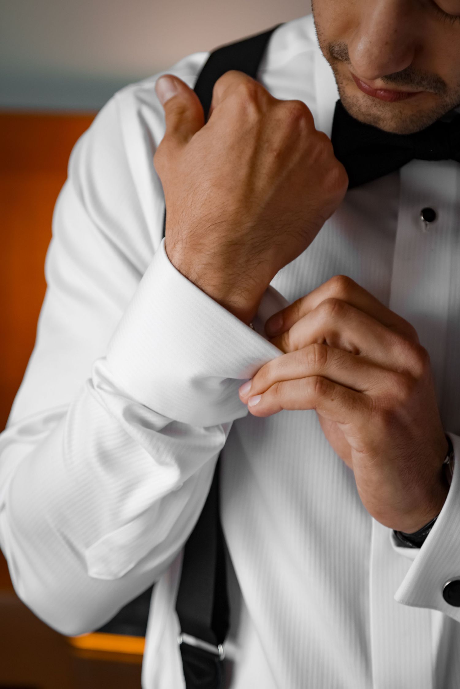 Close up of hands fastening cufflinks on a crisp white tuxedo shirt with black bow tie.