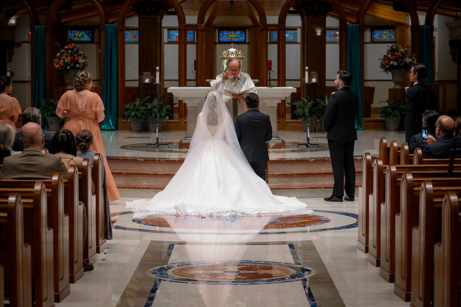 A wedding ceremony takes place in a beautiful church with wooden pews and decorative flowers along the aisle.