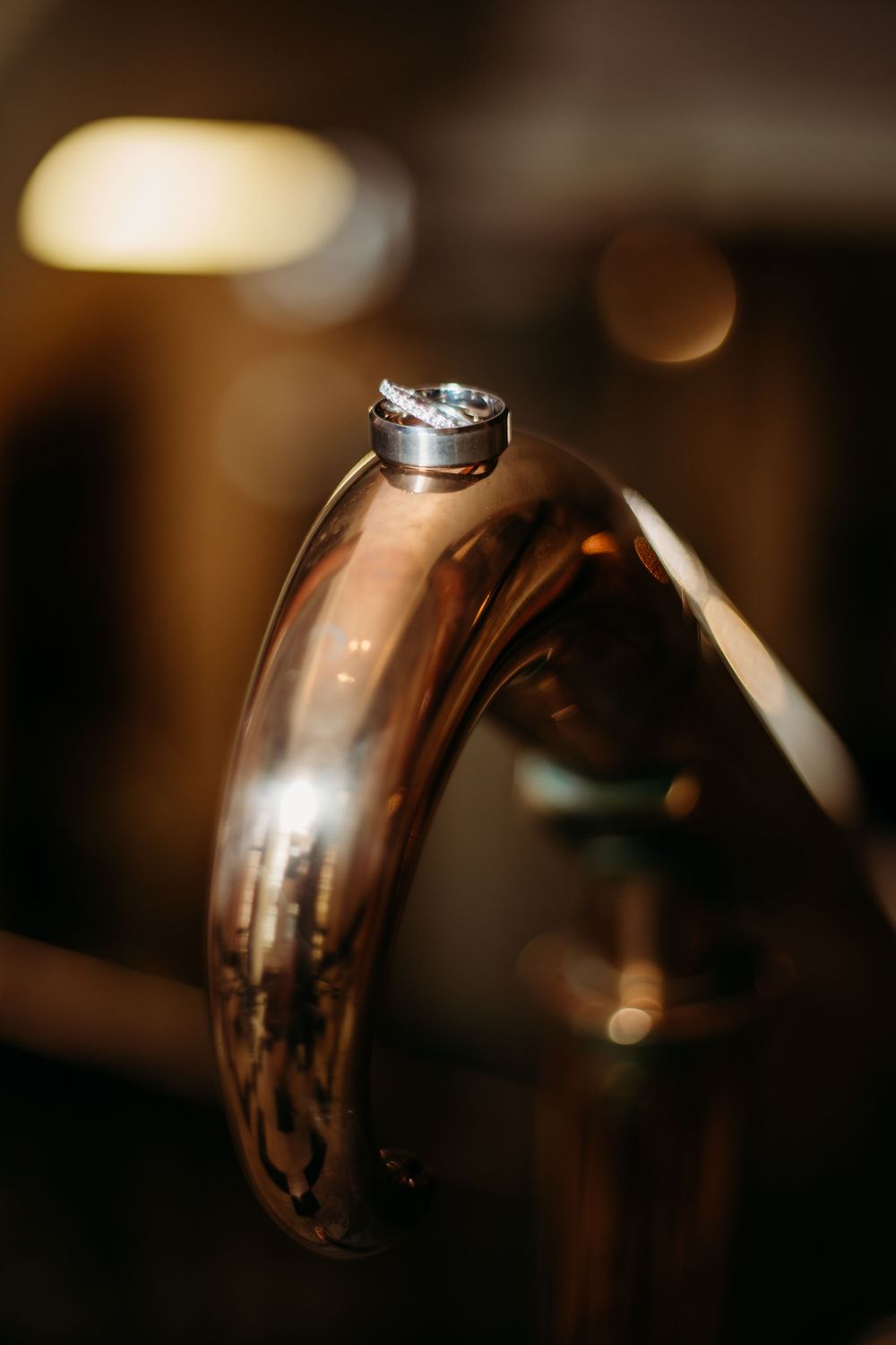 Wedding rings balanced artistically on reflective curved surface with bokeh lighting.