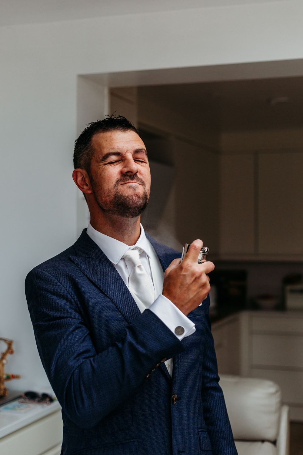 Person in navy suit spraying cologne while getting ready.