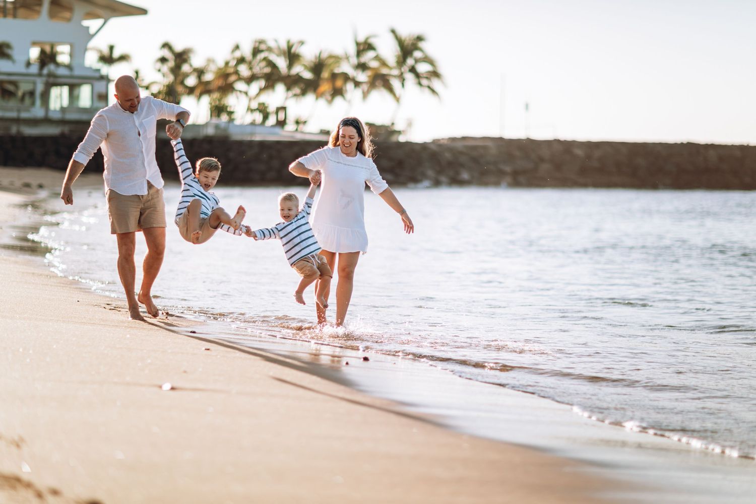 Family of four walking on a beach and holding hands with two small boys suspended in the air.