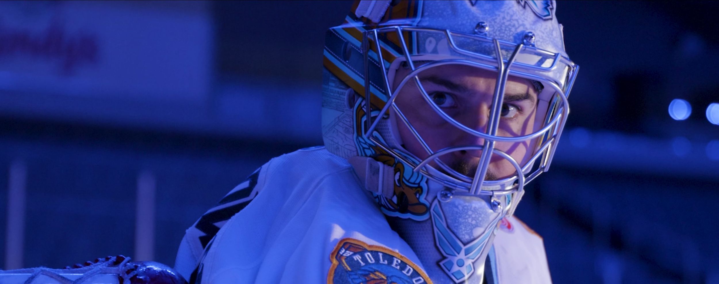 Hockey goalie in protective gear illuminated by blue lighting.