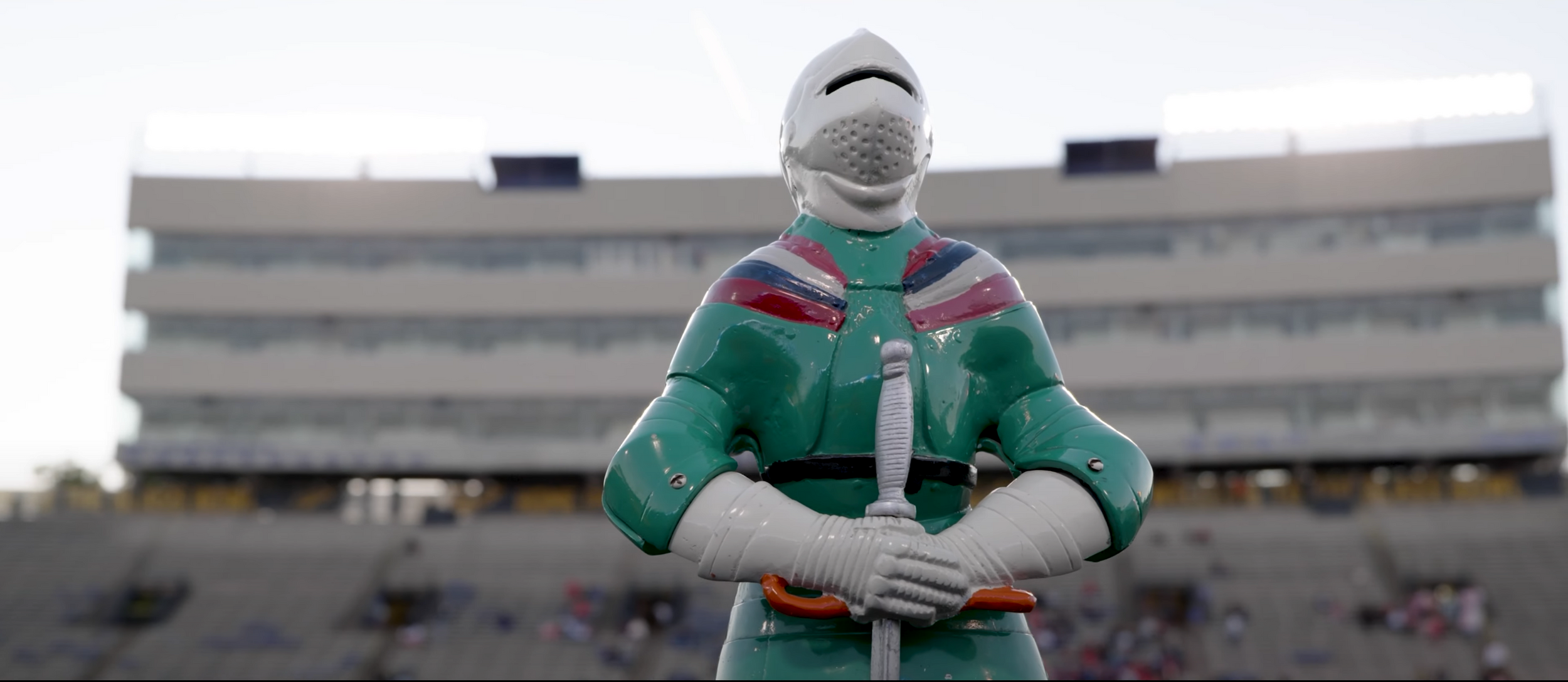 Figure in green uniform standing in empty stadium with crossed arms.
