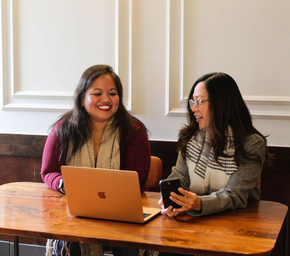 Two people having an animated discussion while working on a laptop at wooden table.