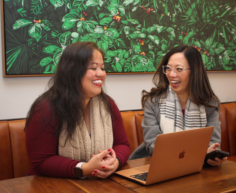 Two colleagues working together with a laptop in front of greenery artwork.