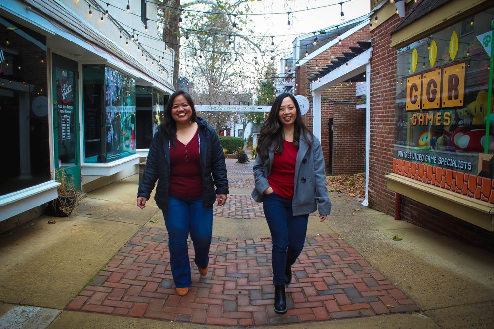 Two friends walking down brick-paved alley between shops.