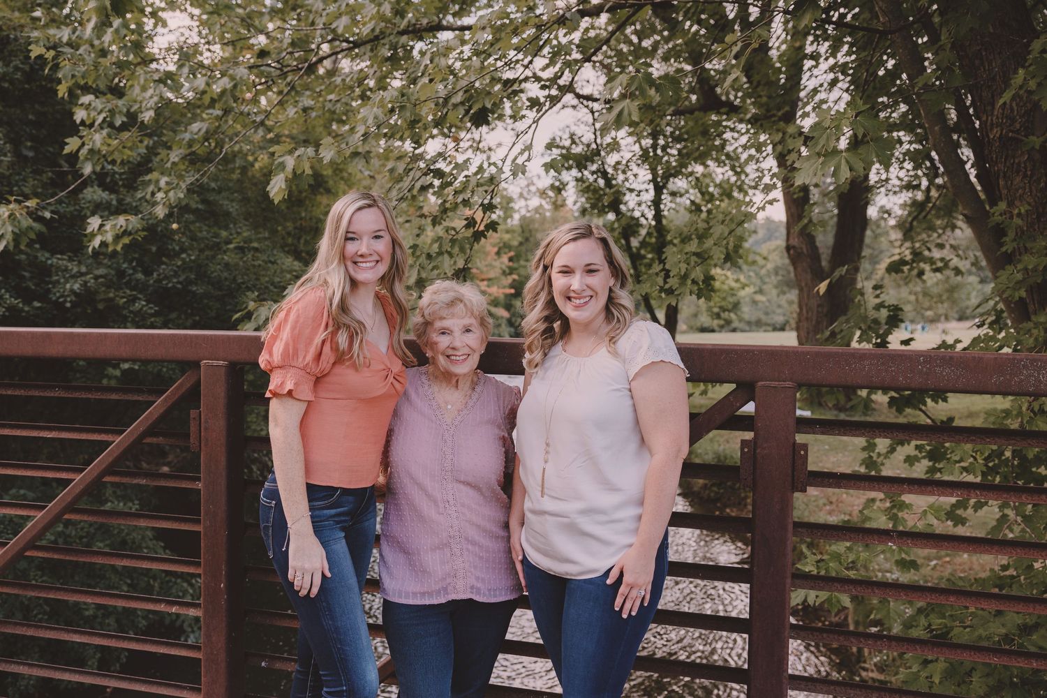 Three individuals wearing casual attire pose together on a wooden bridge during an outdoor photo session.