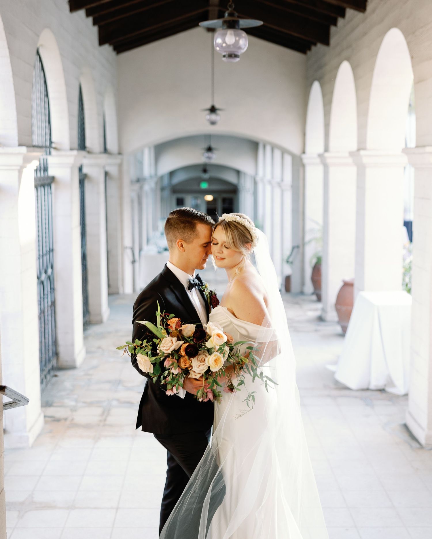 Emotional editorial wedding photography of a groom kissing his bride's forehead in a beautiful arched corridor.