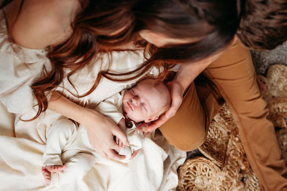 Mother gazing lovingly at her smiling newborn baby lying on a textured blanket.