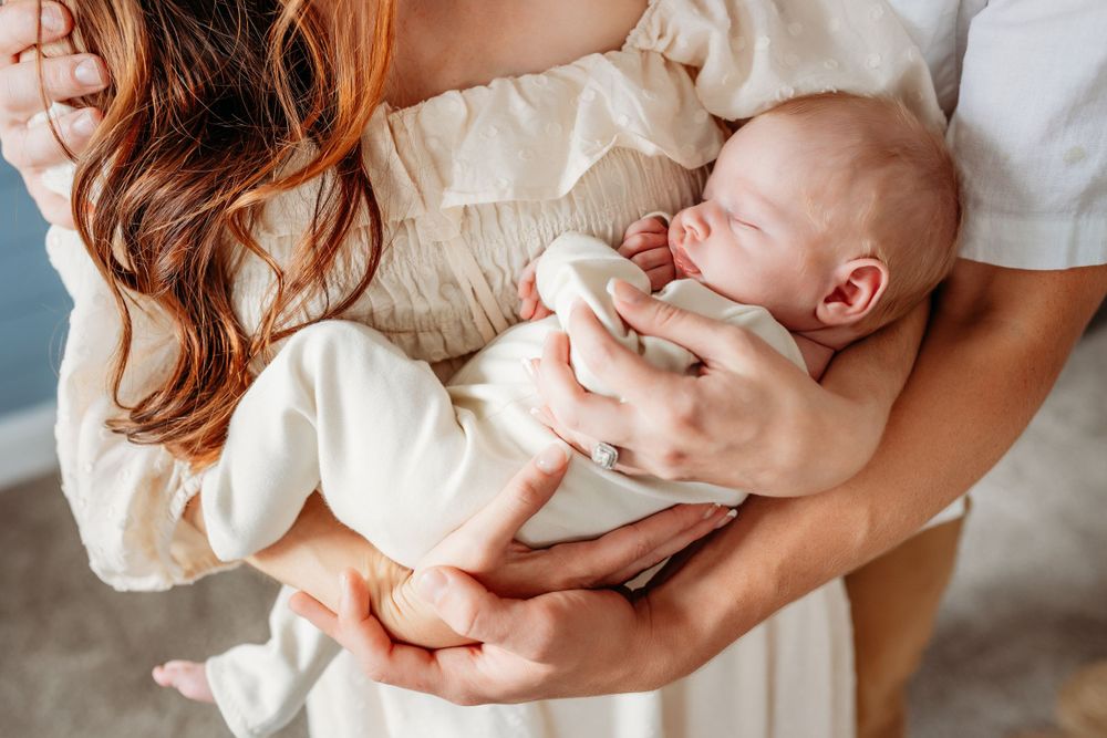Close-up of parents gently cradling a sleeping newborn baby wrapped in white.
