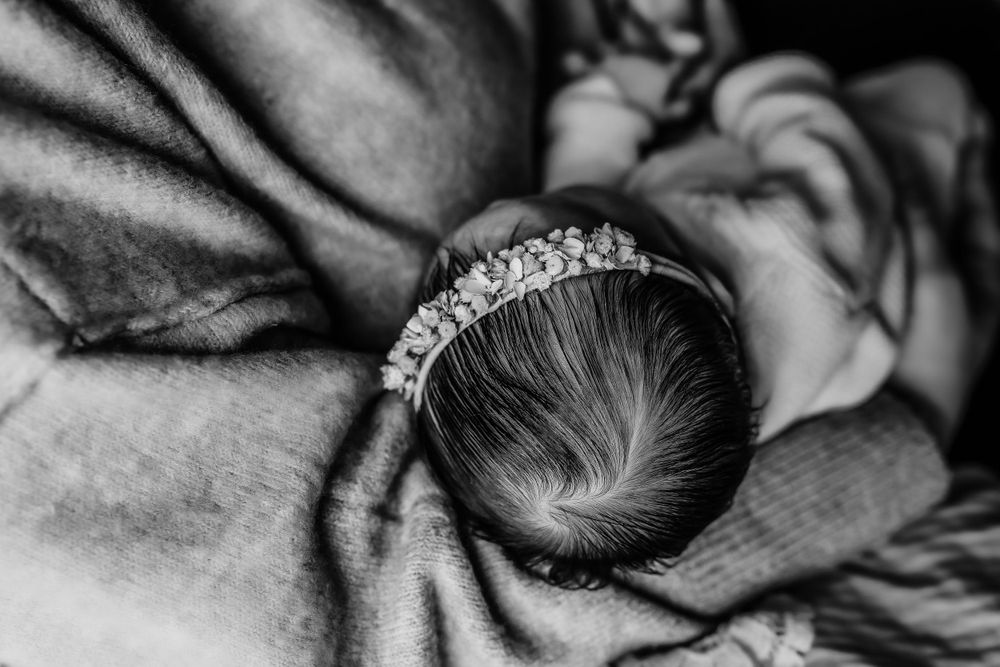Black and white photo of a sleeping newborn baby girl wearing a delicate crystal tiara headband.