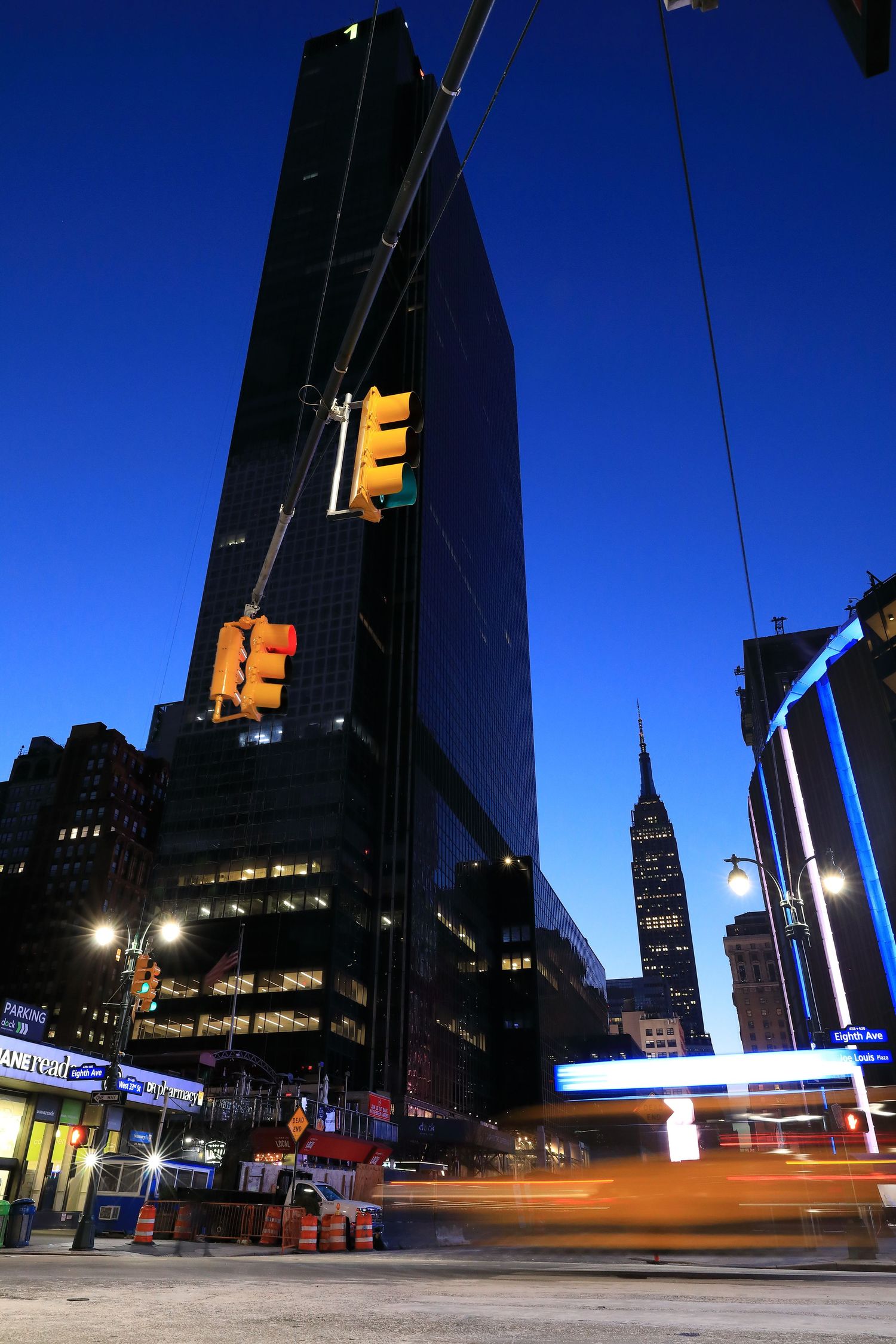 Low angle view of modern skyscraper with traffic lights against blue sky and Empire State Building.
