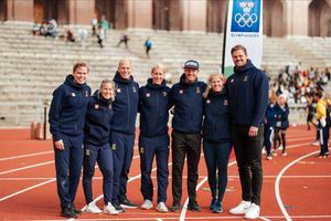 Group photo of athletic team members wearing matching navy uniforms on a track field.