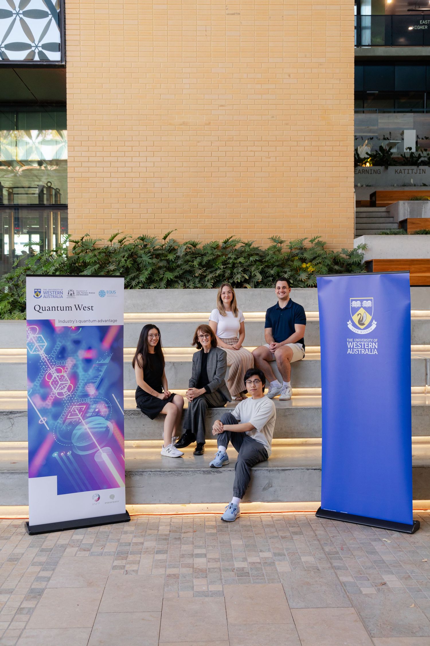 Group poses on outdoor steps with promotional banners at business event.