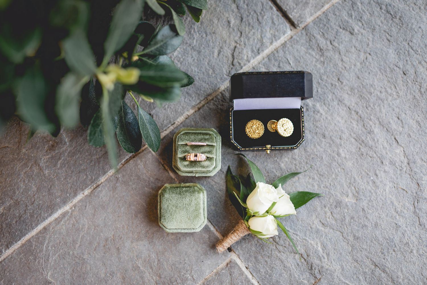 Wedding accessories including vintage ring box and boutonniere laid out on stone surface.