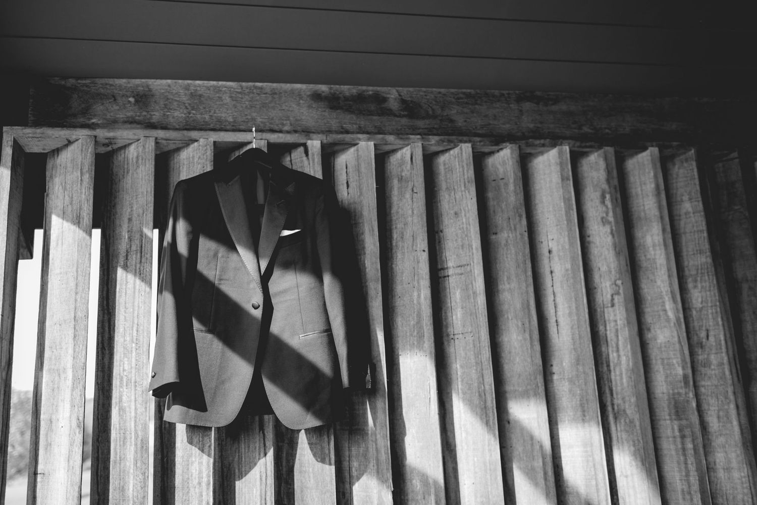 Artistic black and white photograph of formal attire hanging on wooden slats.