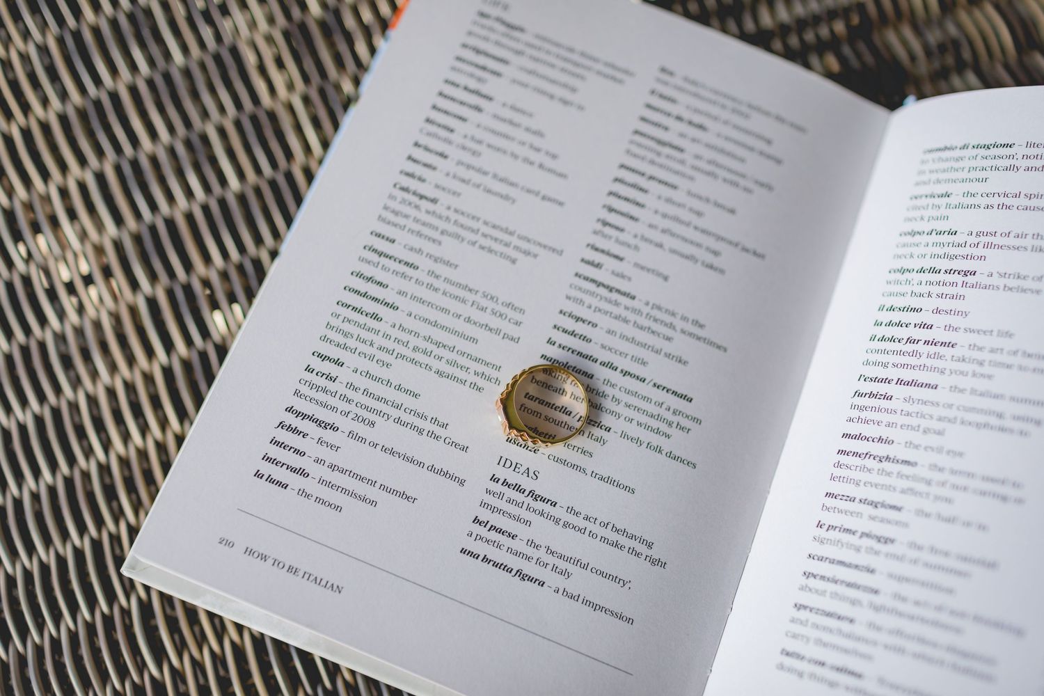 Gold wedding ring photographed on open book pages against woven textured background.