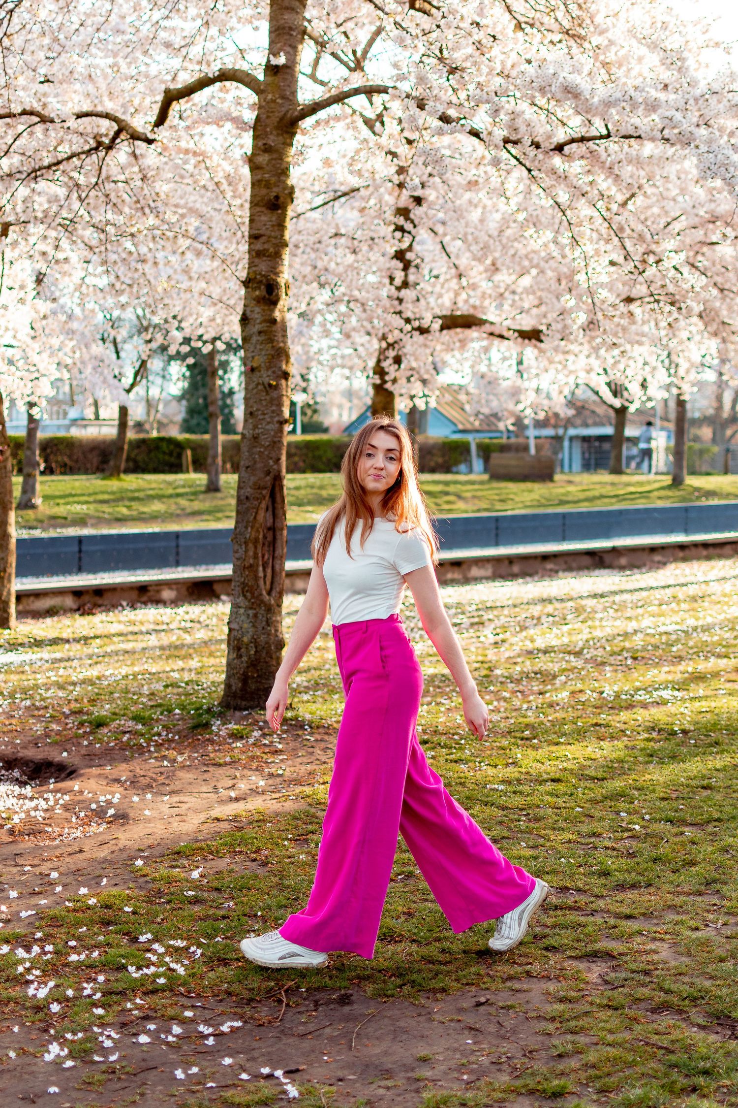 Full-body photo of a woman in pink pants walking in front of flower blooming trees in Spring in Westerpark, Amsterdam