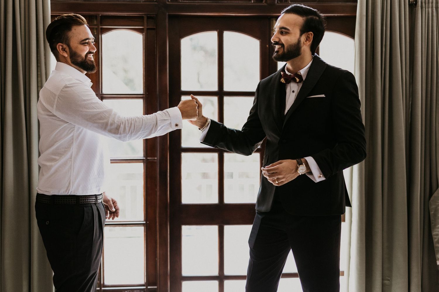 Two people in contrasting formal wear shake hands by a window.