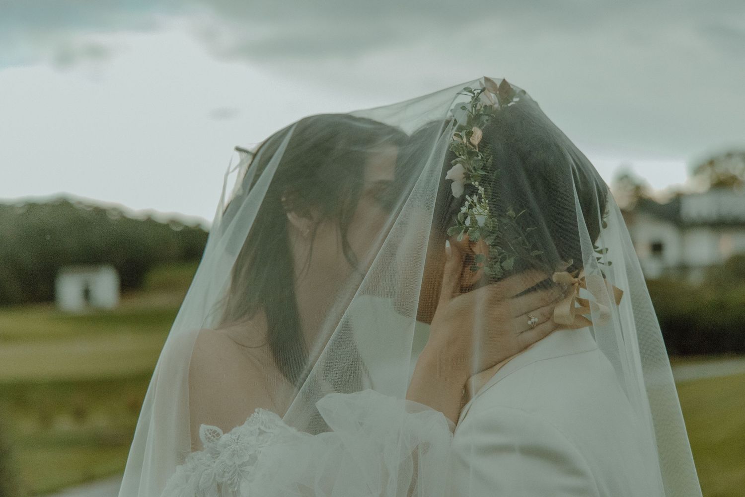 Couple both under the brides veil kissing on their wedding day