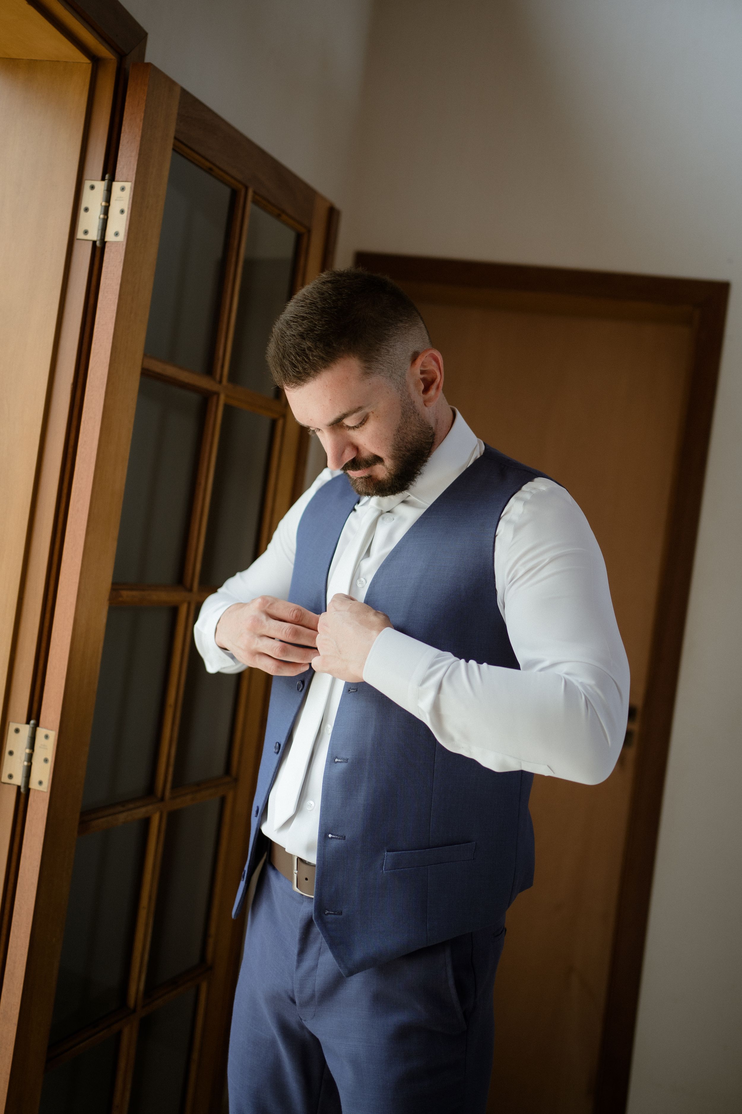 Someone adjusting formal attire while wearing a blue vest and white dress shirt.