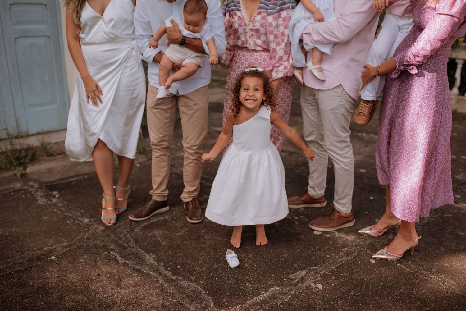 A child in a white dress twirls joyfully while surrounded by people in light colored outfits.
