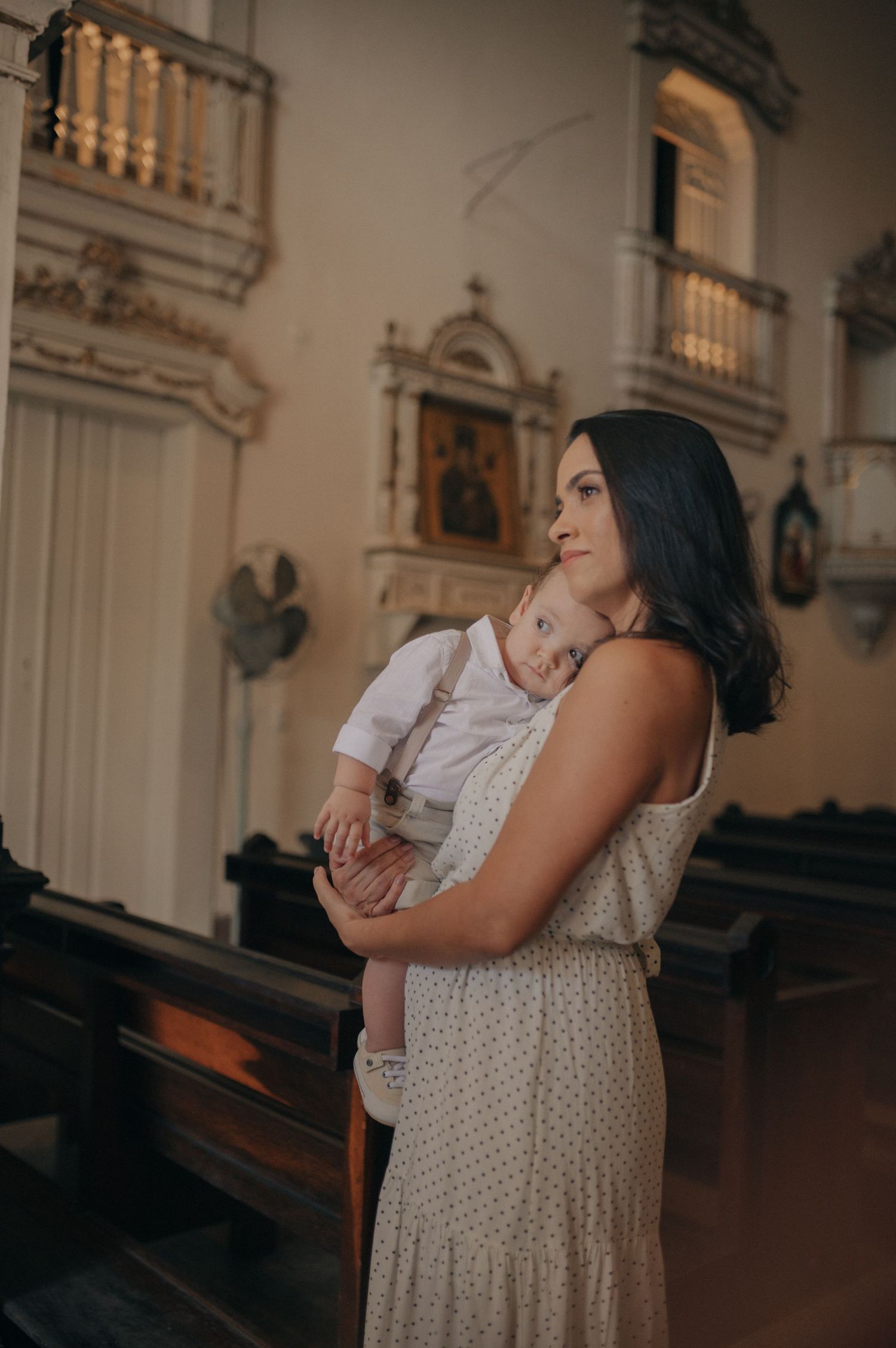 Woman in polka dot dress holds baby inside ornate church interior.