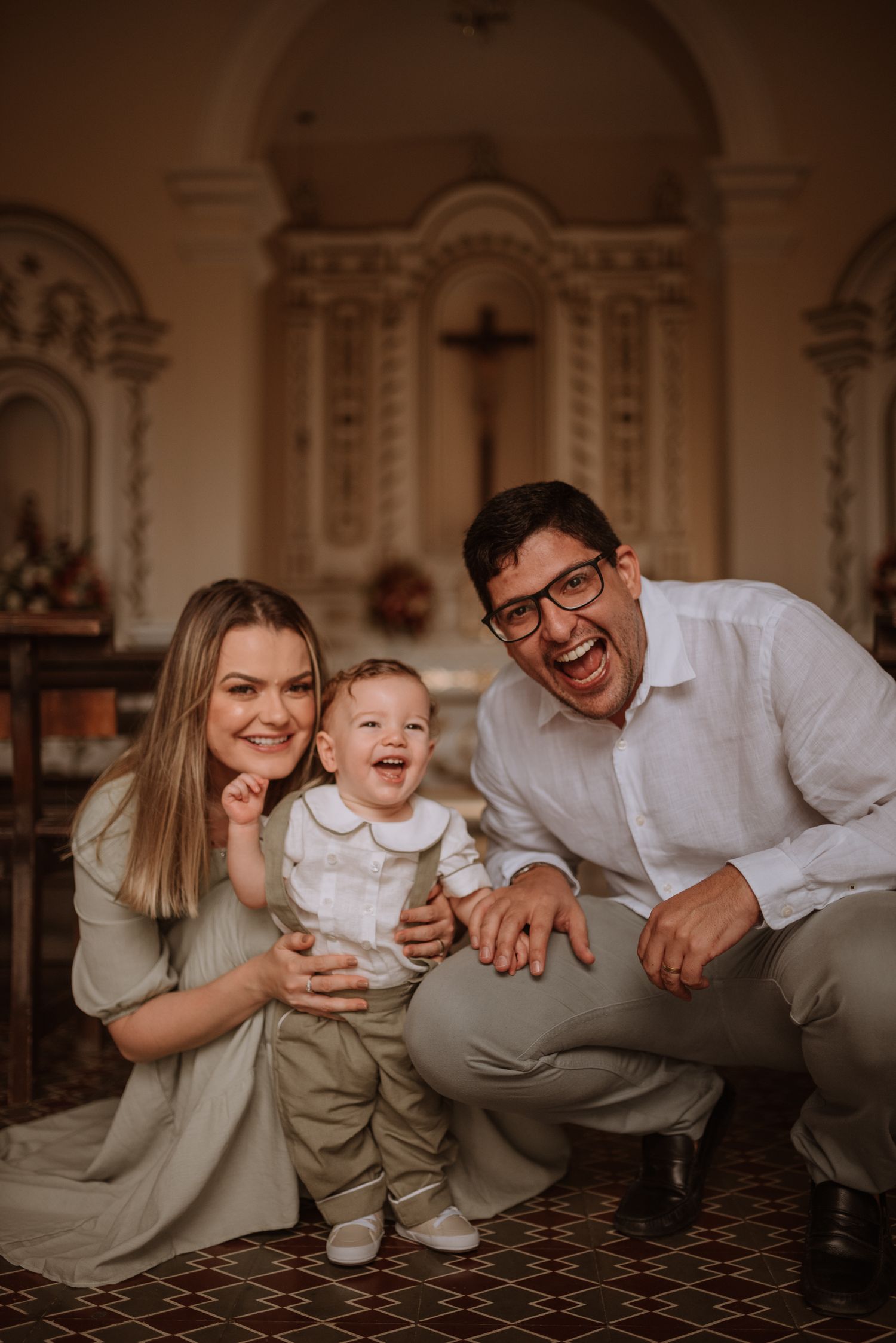 Family of three shares laughing moment together on patterned church floor.