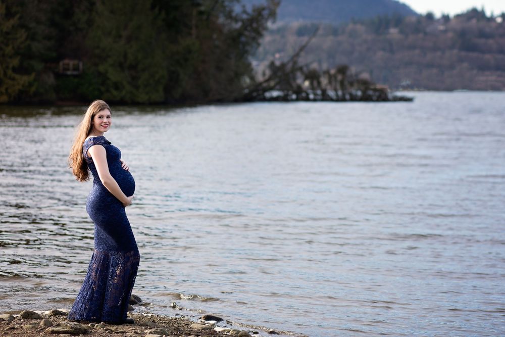 Mom in a beautiful maternity gown overlooks the water.